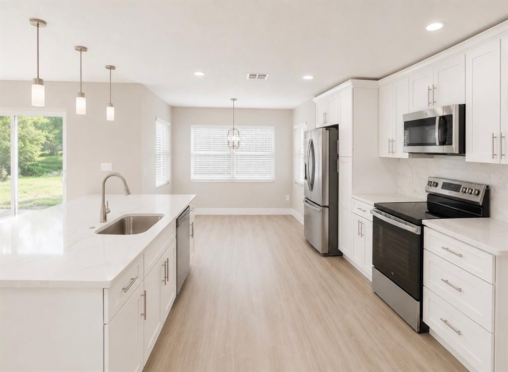 A modern kitchen features white cabinets, stainless steel appliances, a large island, and light flooring — 10814 CRESCENDO LOOP, CLERMONT, FL