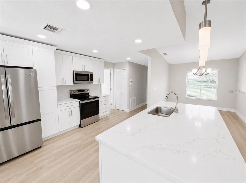 A modern kitchen features white cabinets, stainless steel appliances, and a large quartz-topped island — 10814 CRESCENDO LOOP, CLERMONT, FL
