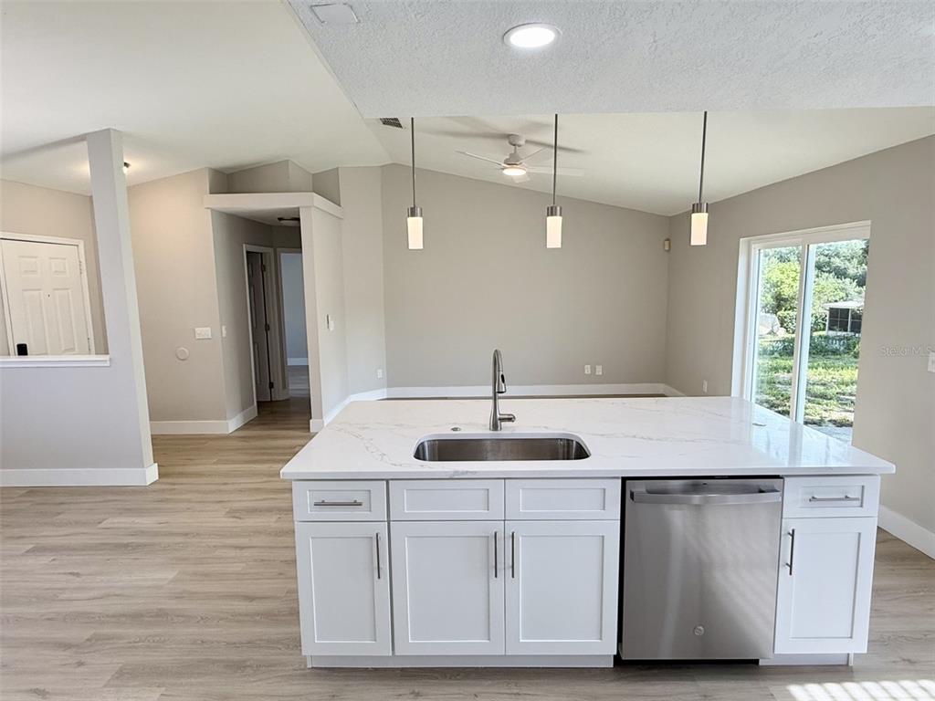A kitchen island with a white marble countertop and stainless steel sink faces a living area — 10814 CRESCENDO LOOP, CLERMONT, FL