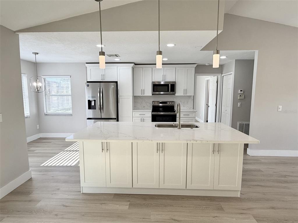 A kitchen features white cabinets, a large island with a quartz countertop, and stainless appliances — 10814 CRESCENDO LOOP, CLERMONT, FL