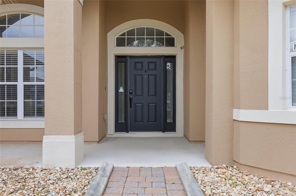 A dark front door with sidelights and a transom window sits under a covered entryway — 2901 SWEETSPIRE CIRCLE, KISSIMMEE, FL