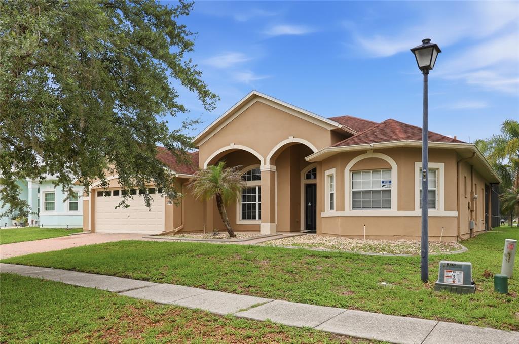 A tan, single-story suburban house with a two-car garage and a front-facing arched entryway — 2901 SWEETSPIRE CIRCLE, KISSIMMEE, FL