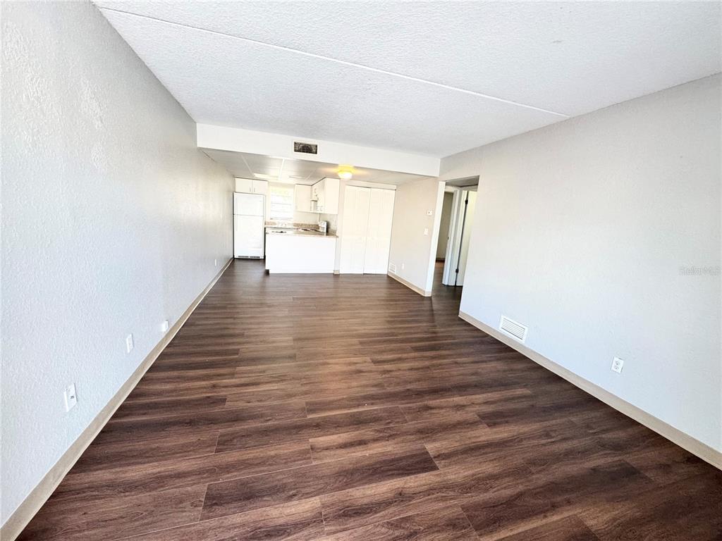A living area with wood-look flooring leads to an open kitchen with white cabinets — 1229 KENNEDY ROAD UNIT 68, DAYTONA BEACH, FL