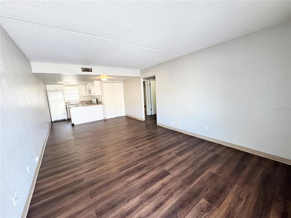 An open-concept living area features wood-look flooring and an adjacent kitchen with white cabinets — 1229 KENNEDY ROAD UNIT 68, DAYTONA BEACH, FL