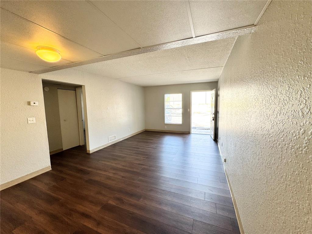An empty room features dark wood-look flooring, white textured walls, and a ceiling-mounted light fixture — 1229 KENNEDY ROAD UNIT 68, DAYTONA BEACH, FL