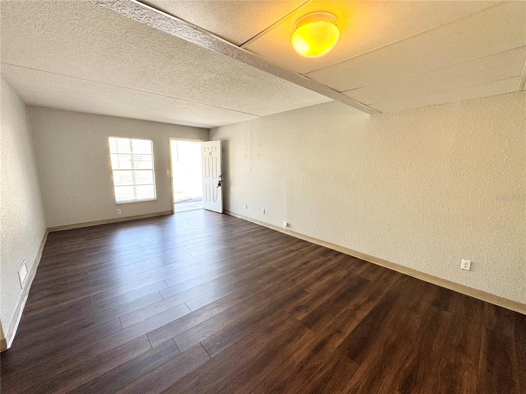 An empty room features dark wood-look flooring, white walls, a drop ceiling, and an exterior door — 1229 KENNEDY ROAD UNIT 68, DAYTONA BEACH, FL