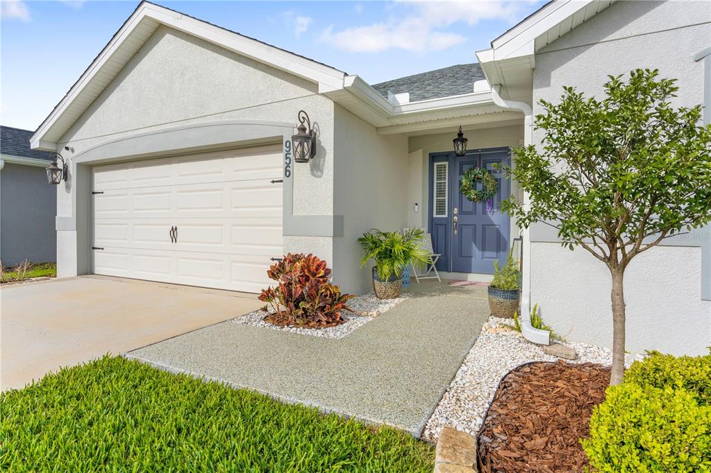A light-colored house exterior features a garage, a blue front door, and a landscaped walkway — 956 ARUBA AVENUE, MULBERRY, FL