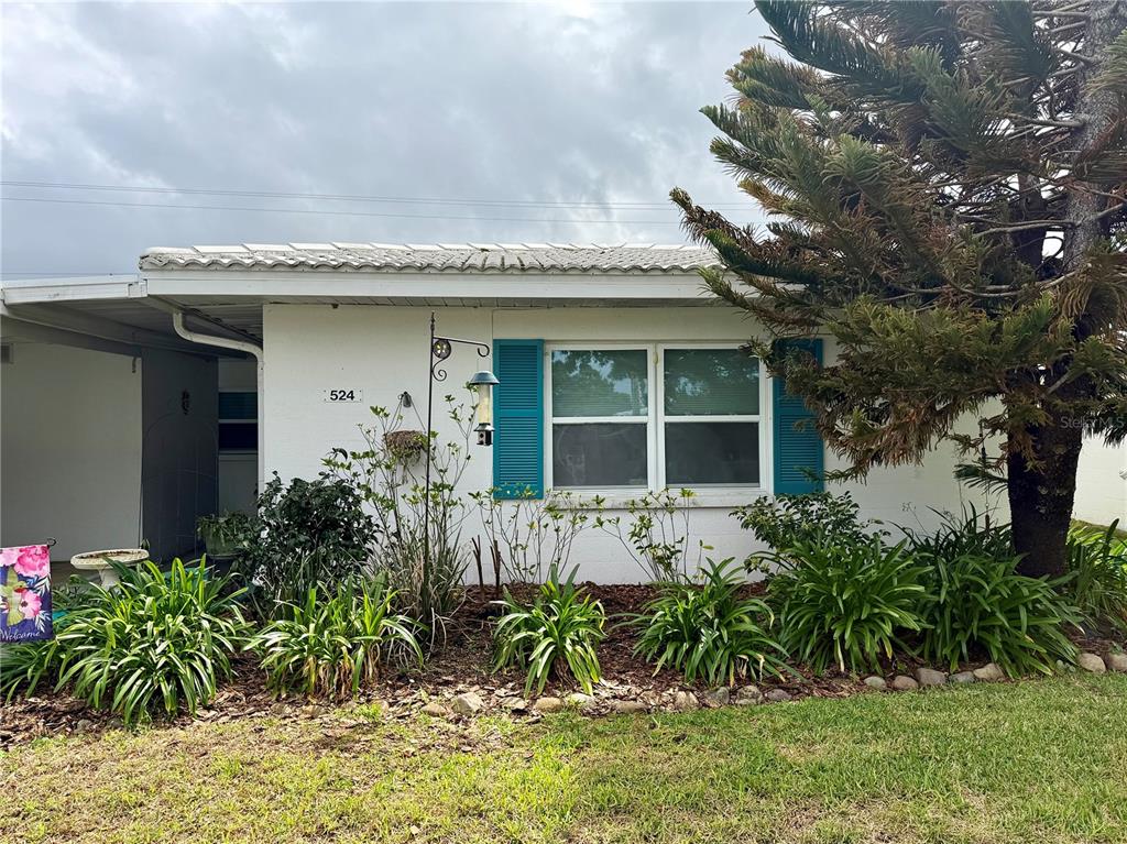 A single-story white house with blue shutters and a front garden under a cloudy sky — 524 CAMEO DRIVE, LAKELAND, FL