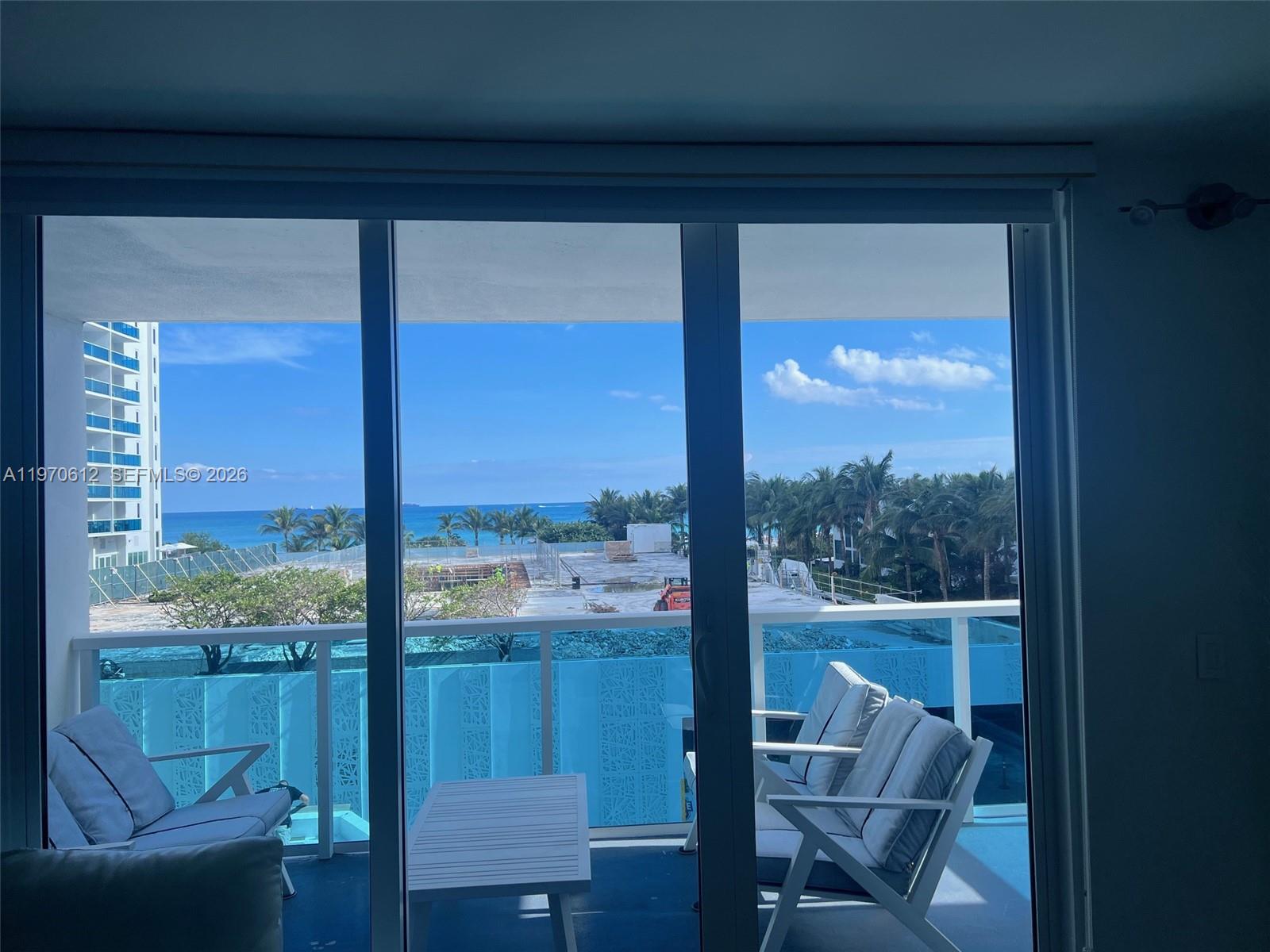A bright living room features white leather sofas, mirrored walls, and a balcony with water views — 2301 Collins Ave # 338, Miami Beach FL 33139, MIAMI BEACH, FL