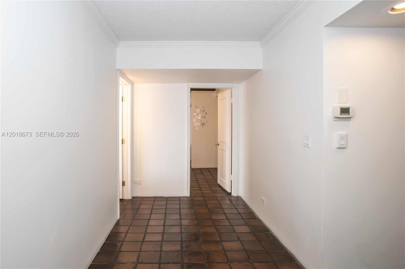 A hallway with brown tile flooring leads to two doorways in a white interior — 1800 NE 114th St # 1207, Miami FL 33181, MIAMI, FL