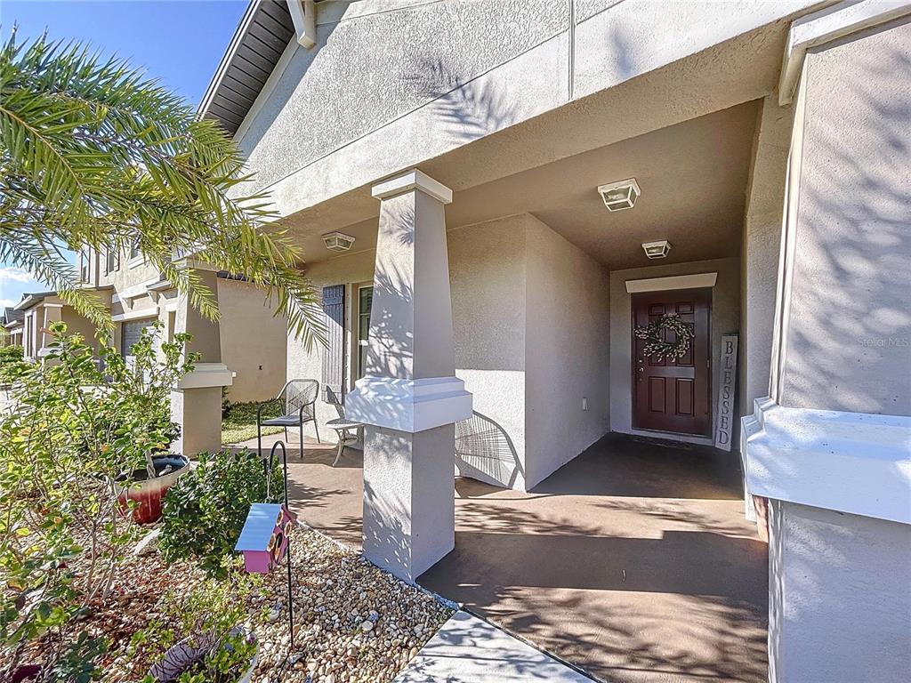 A covered front porch features a brown door, stone pillars, and a small seating area — 197 RAIN BERRY AVENUE, RUSKIN, FL