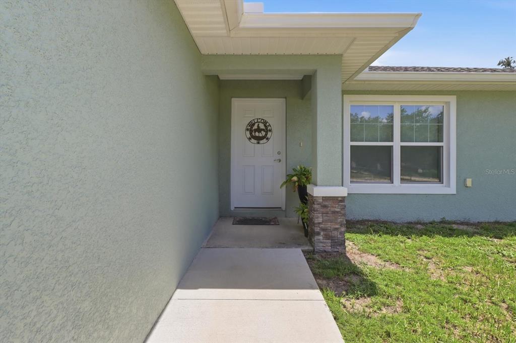 A concrete walkway leads to the front door of a light green house with stone accents — 13730 SW 102ND STREET, DUNNELLON, FL