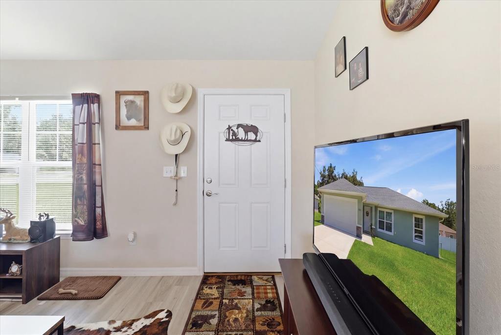 A living room features a white front door, cowboy hats, and a television on a stand — 13730 SW 102ND STREET, DUNNELLON, FL