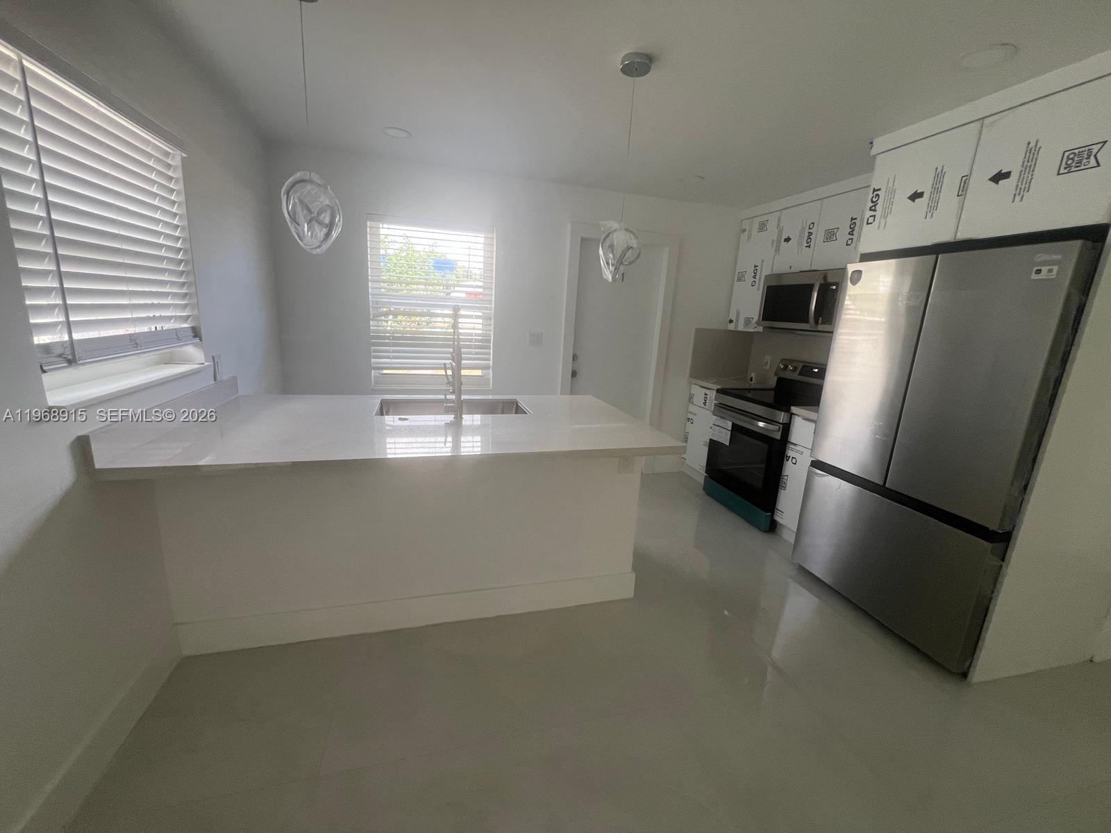 A modern kitchen features white cabinetry, a quartz island with a sink, and stainless appliances — 361 NW 16th St, Pompano Beach FL 33060, POMPANO BEACH, FL