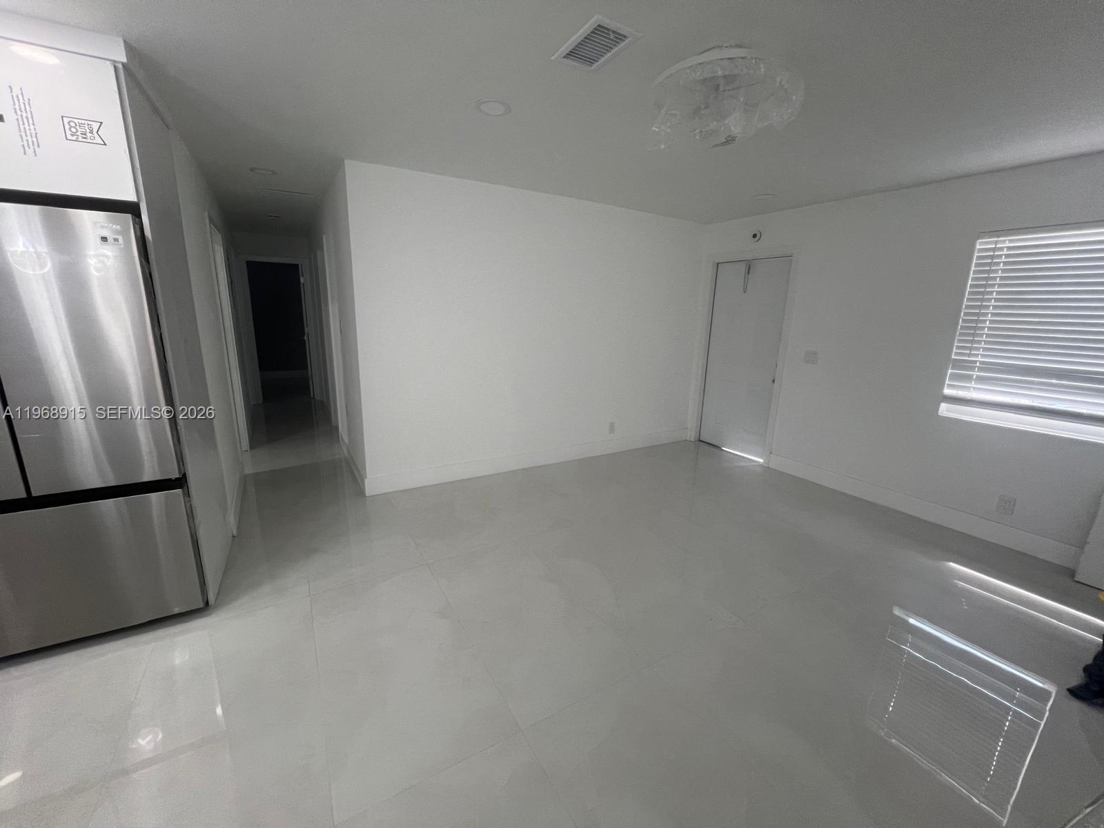 A bright, empty room features white walls, glossy tile flooring, a stainless refrigerator, and a window — 361 NW 16th St, Pompano Beach FL 33060, POMPANO BEACH, FL