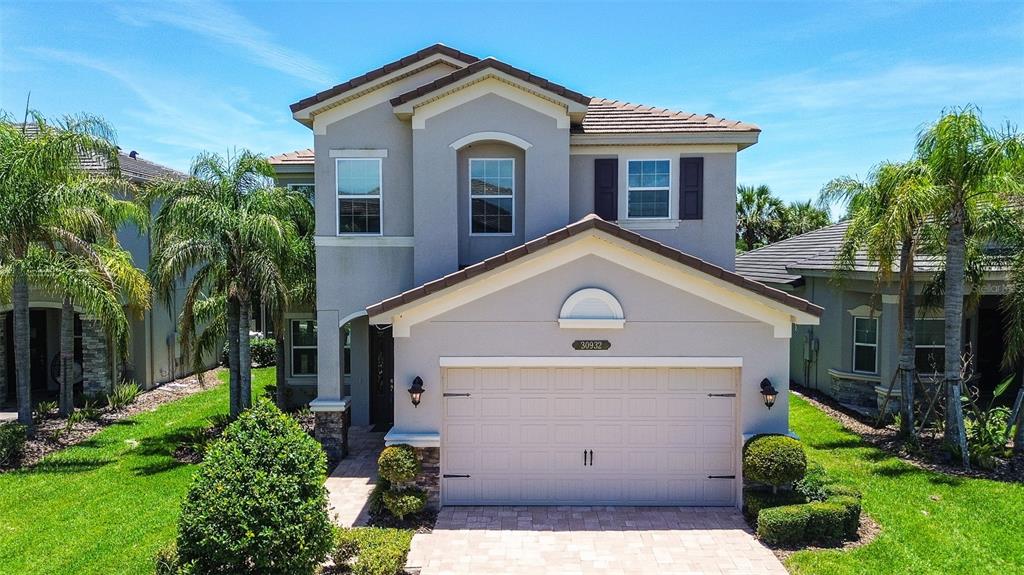 A two-story suburban house with a beige stucco exterior, a tiled roof, and a garage — 30932 LINDENTREE DRIVE, WESLEY CHAPEL, FL