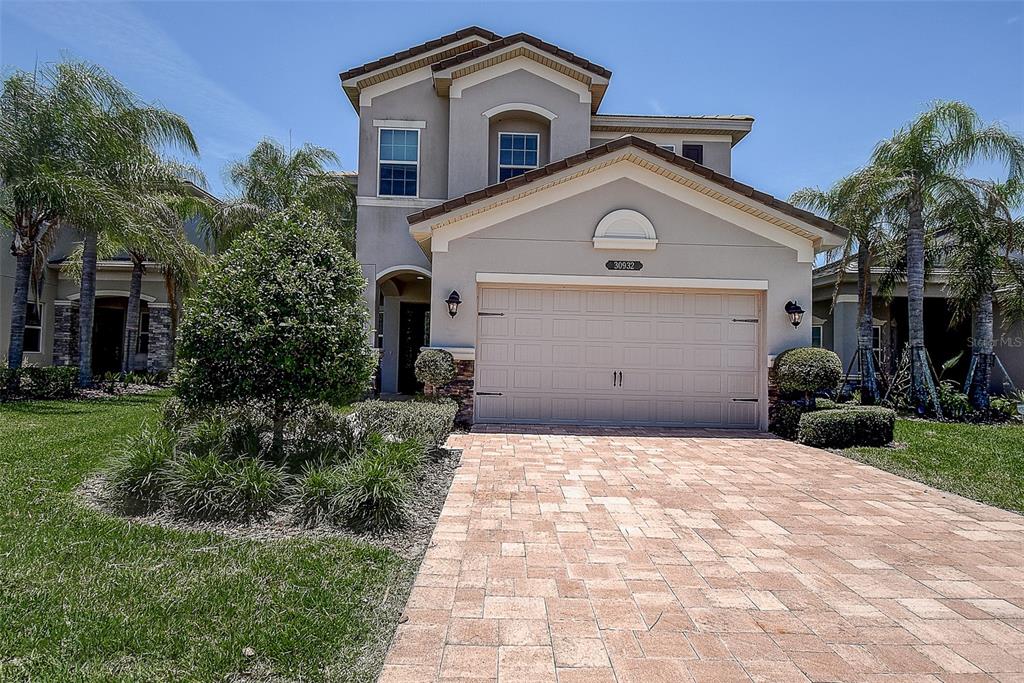 A two-story house with a beige stucco exterior, a paved driveway, and palm trees — 30932 LINDENTREE DRIVE, WESLEY CHAPEL, FL