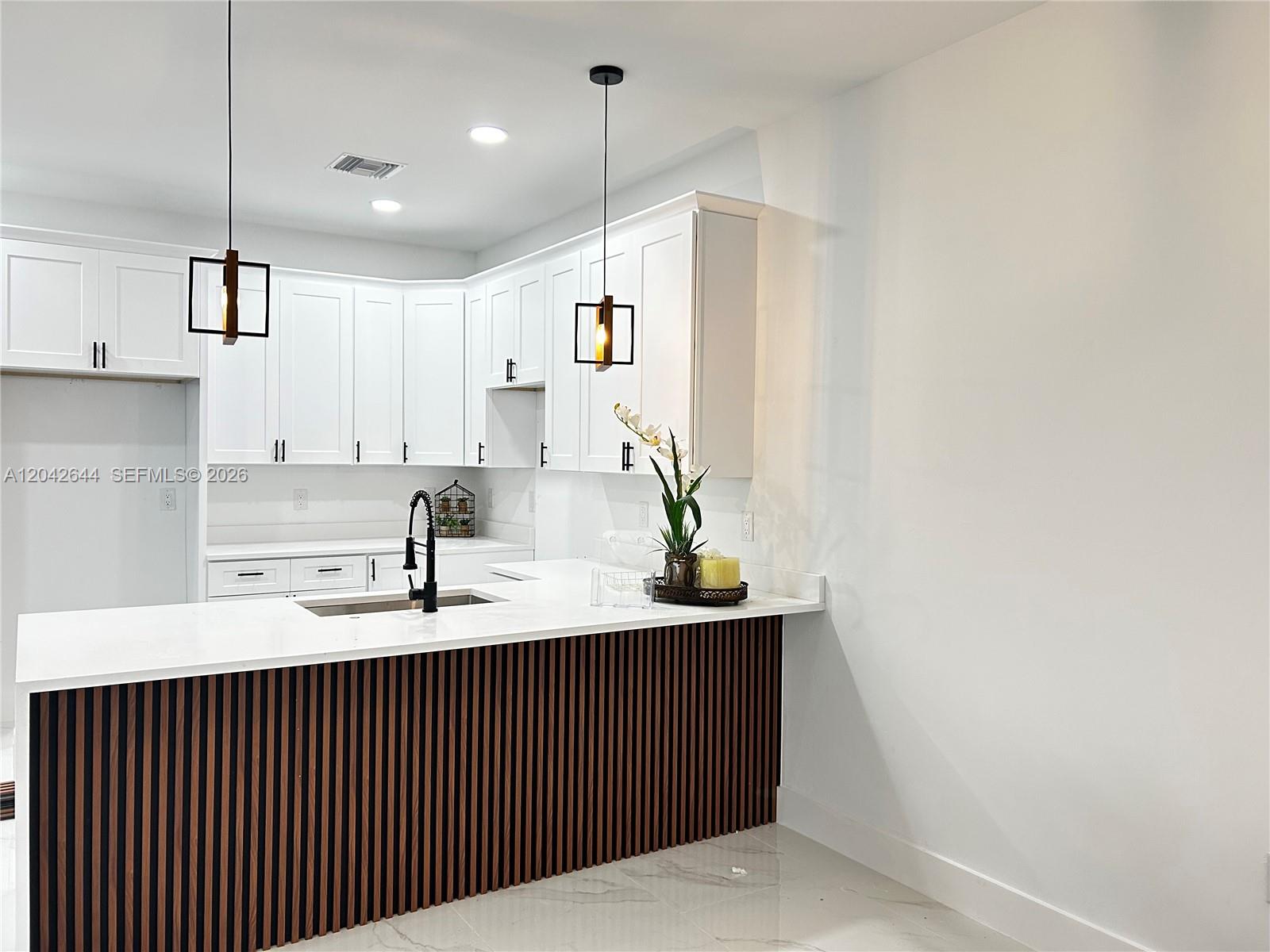 A modern kitchen features white cabinets, a slatted wood island, and black pendant lights — 1117 Hudson, Lehigh Acres FL 33974, LEHIGH ACRES, FL