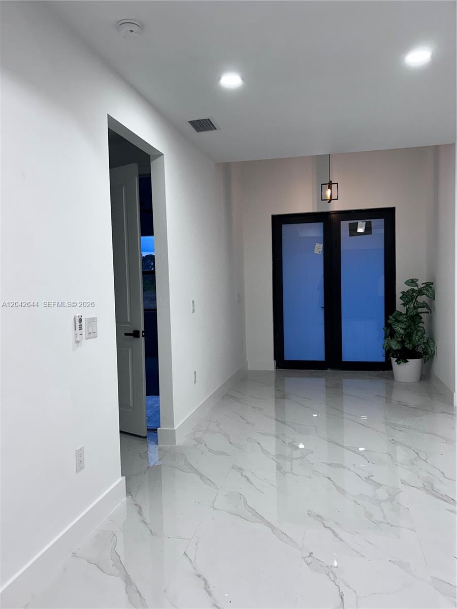 A bright entryway features white marble-look tile flooring, white walls, and black-framed glass doors — 1117 Hudson, Lehigh Acres FL 33974, LEHIGH ACRES, FL