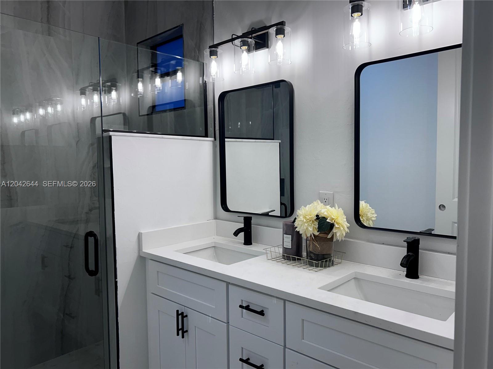 A modern bathroom features a double vanity with white cabinets, black hardware, and two mirrors — 1117 Hudson, Lehigh Acres FL 33974, LEHIGH ACRES, FL