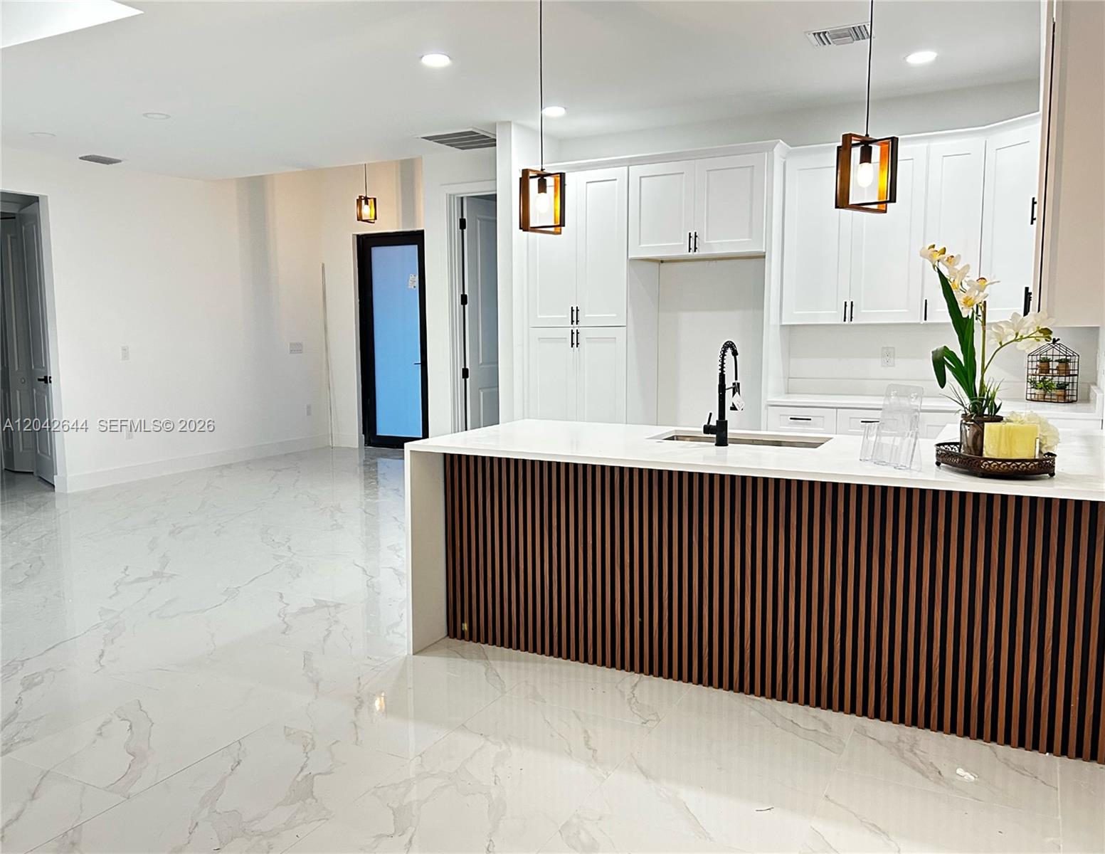 A modern kitchen features white cabinetry, a slatted wood island, and white marble-look flooring — 1117 Hudson, Lehigh Acres FL 33974, LEHIGH ACRES, FL
