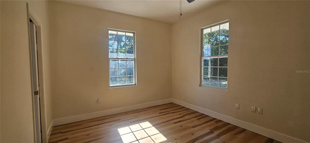 An empty bedroom features light-colored walls, wood-look flooring, and two windows — 709 S HIGHLAND STREET, MOUNT DORA, FL