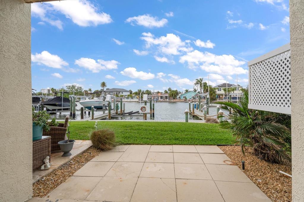 A patio with stone pavers overlooks a grassy lawn, a boat dock, and a canal — 124 MARCDALE BOULEVARD, INDIAN ROCKS BEACH, FL