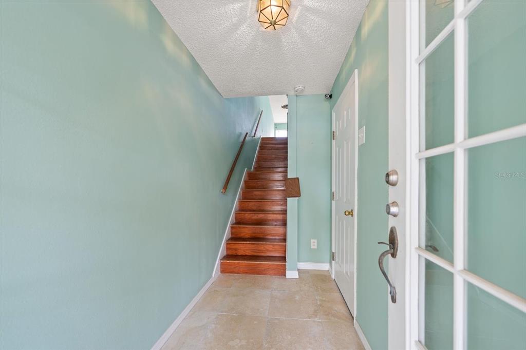 An entryway features light green walls, tiled flooring, and a wooden staircase leading upstairs — 124 MARCDALE BOULEVARD, INDIAN ROCKS BEACH, FL