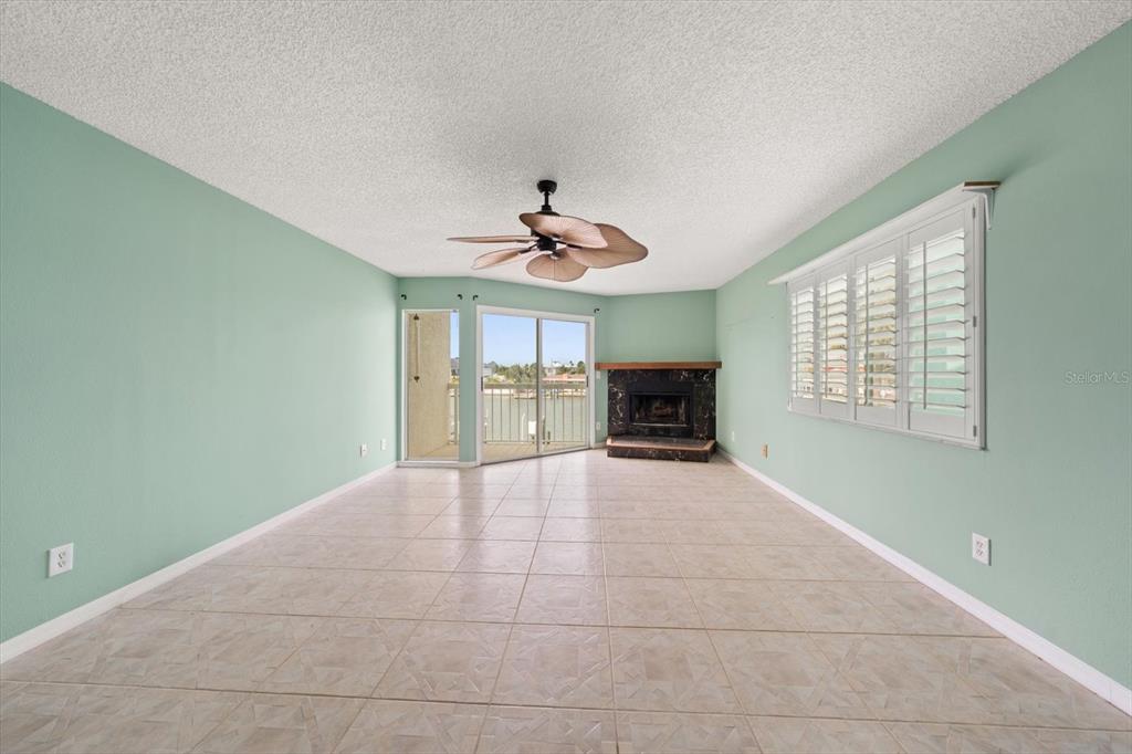 A living room with light green walls, tile flooring, a fireplace, and a sliding door — 124 MARCDALE BOULEVARD, INDIAN ROCKS BEACH, FL
