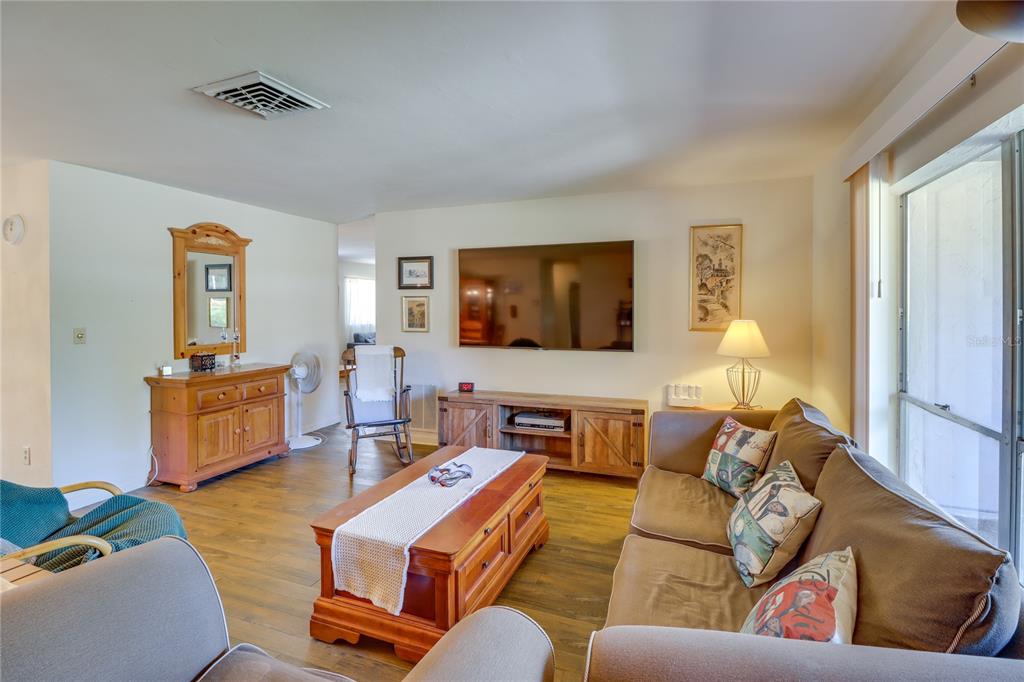 A living room features wood flooring, a wooden coffee table, a sofa, and a wall-mounted television — 20790 SW 88TH PLACE ROAD, DUNNELLON, FL