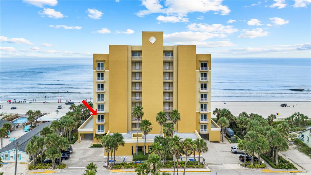 An exterior view of a yellow multi-story beachfront condominium building with a red arrow pointing toward a balcony — 1705 S ATLANTIC AVENUE UNIT 301, NEW SMYRNA BEACH, FL