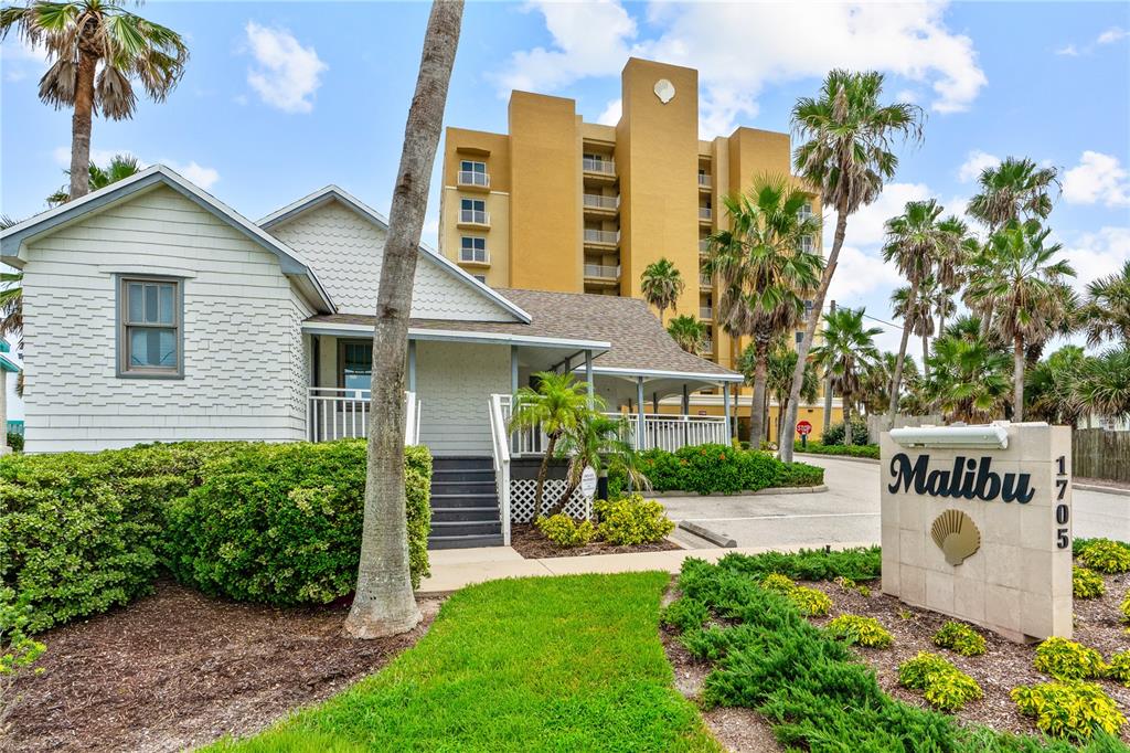 A white cottage stands in front of a tall yellow apartment building with palm trees — 1705 S ATLANTIC AVENUE UNIT 301, NEW SMYRNA BEACH, FL