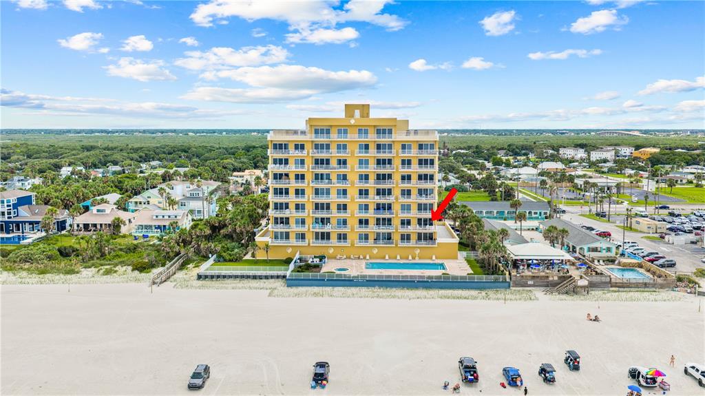 An aerial view shows a multi-story yellow beachfront condominium building with a pool and parking — 1705 S ATLANTIC AVENUE UNIT 301, NEW SMYRNA BEACH, FL