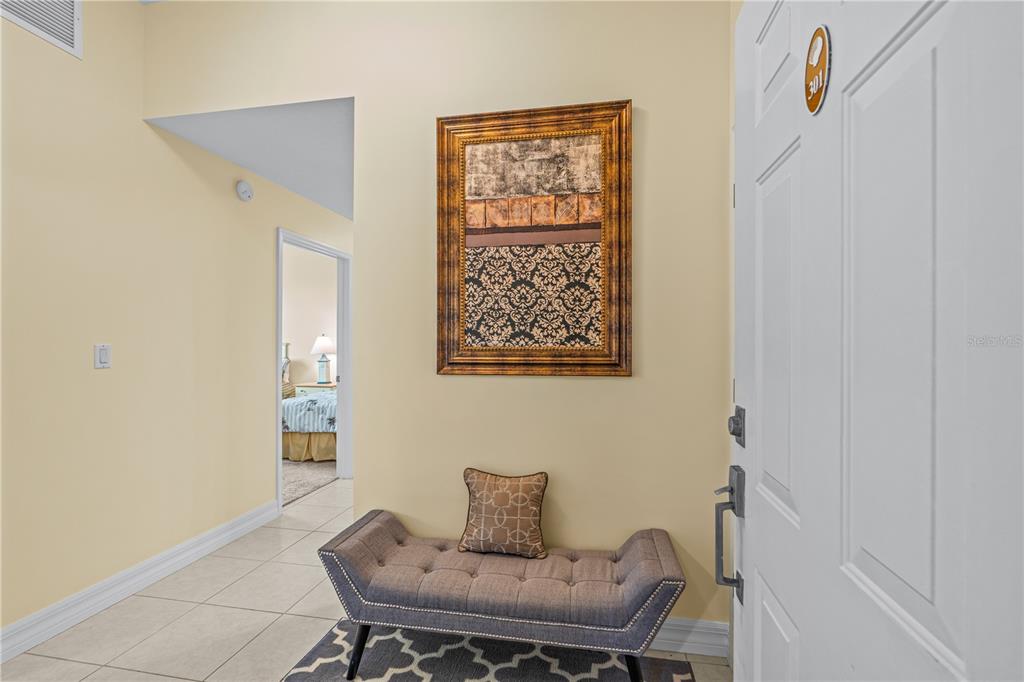 An entryway features a tufted bench, a framed wall art piece, and a tiled floor — 1705 S ATLANTIC AVENUE UNIT 301, NEW SMYRNA BEACH, FL