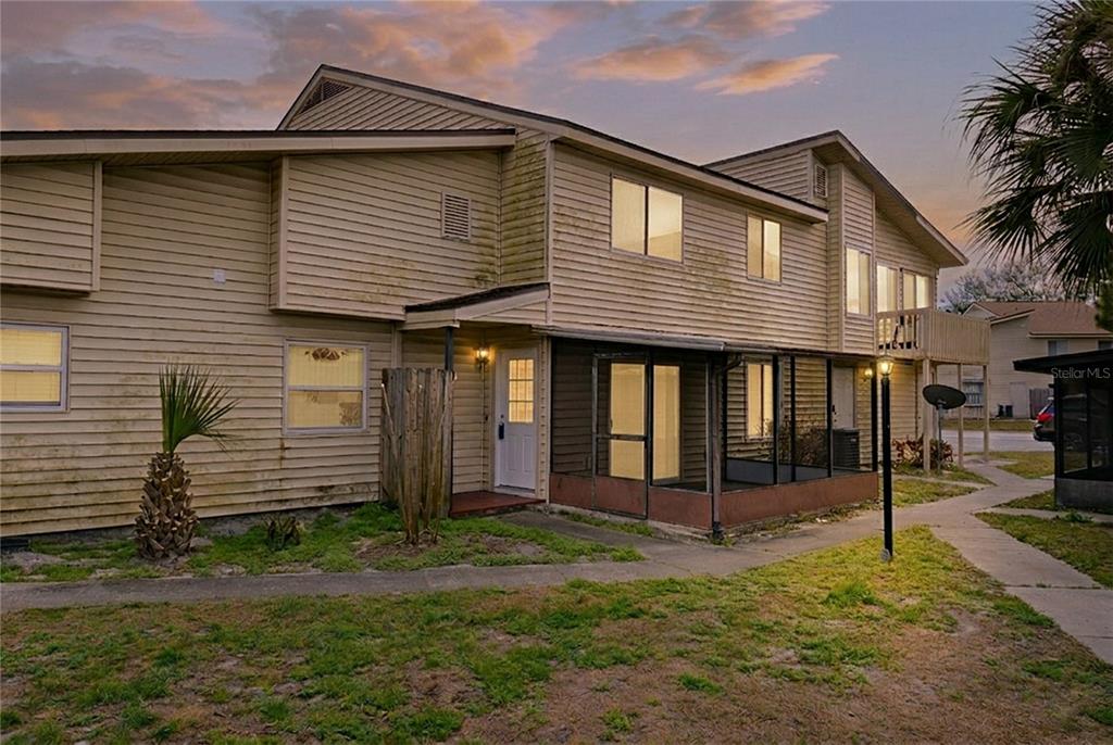 A two-story residential building with light-colored siding, a screened-in porch, and a small front yard — 1023 SPRING MEADOW DRIVE UNIT 1023, KISSIMMEE, FL