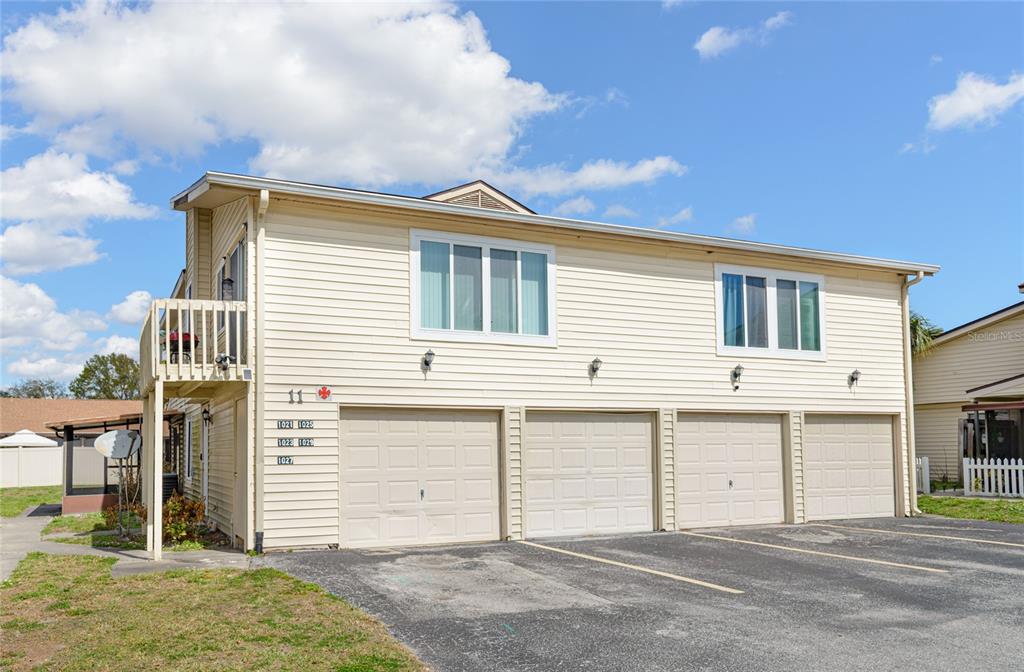 A two-story building with beige siding features three garage doors and an upper-level balcony — 1023 SPRING MEADOW DRIVE UNIT 1023, KISSIMMEE, FL