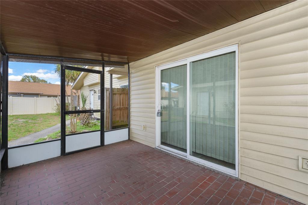 A screened-in patio features a brick floor, wood-paneled ceiling, and sliding glass doors — 1023 SPRING MEADOW DRIVE UNIT 1023, KISSIMMEE, FL