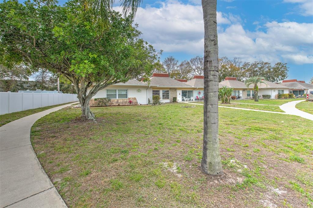 A row of single-story residential units with brown roofs sits behind a grassy lawn — 4313 TAHITIAN GARDENS CIRCLE UNIT A, HOLIDAY, FL