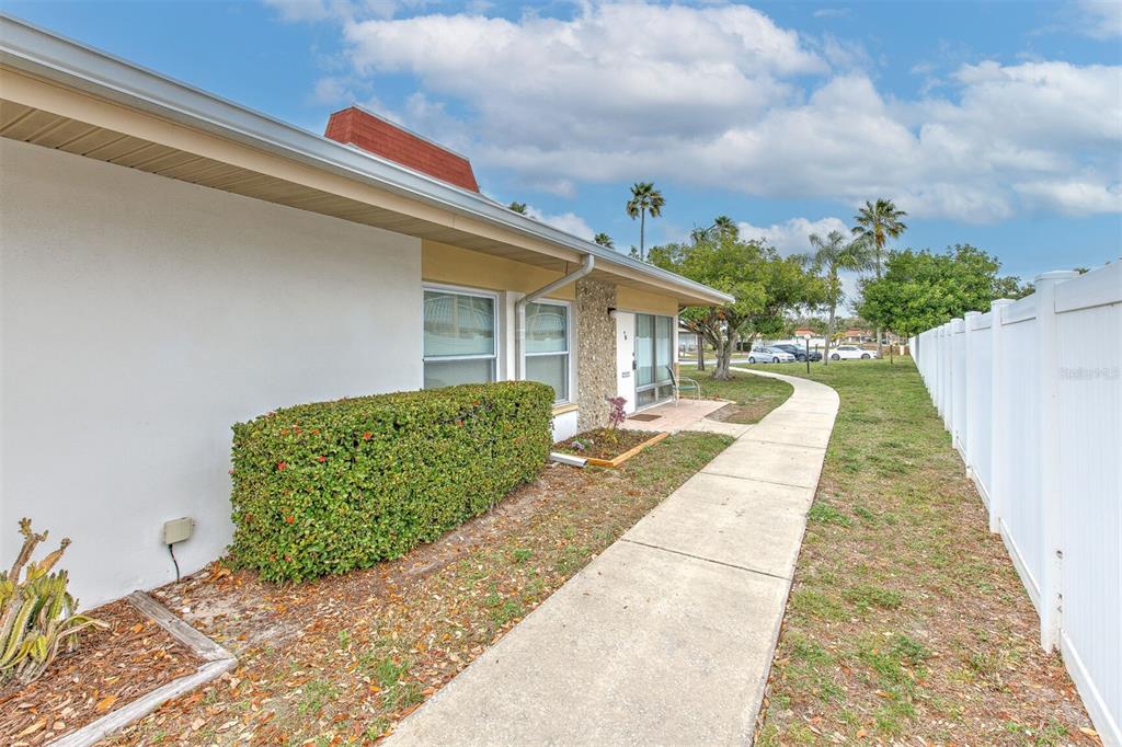A white house exterior features a concrete walkway, a manicured hedge, and a vinyl fence — 4313 TAHITIAN GARDENS CIRCLE UNIT A, HOLIDAY, FL