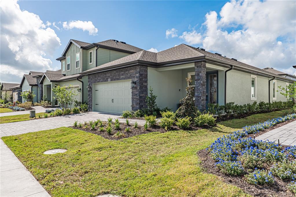 A light green house with a stone-accented garage and a covered entryway under a blue sky — 7753 SOMERSWORTH DRIVE, KISSIMMEE, FL