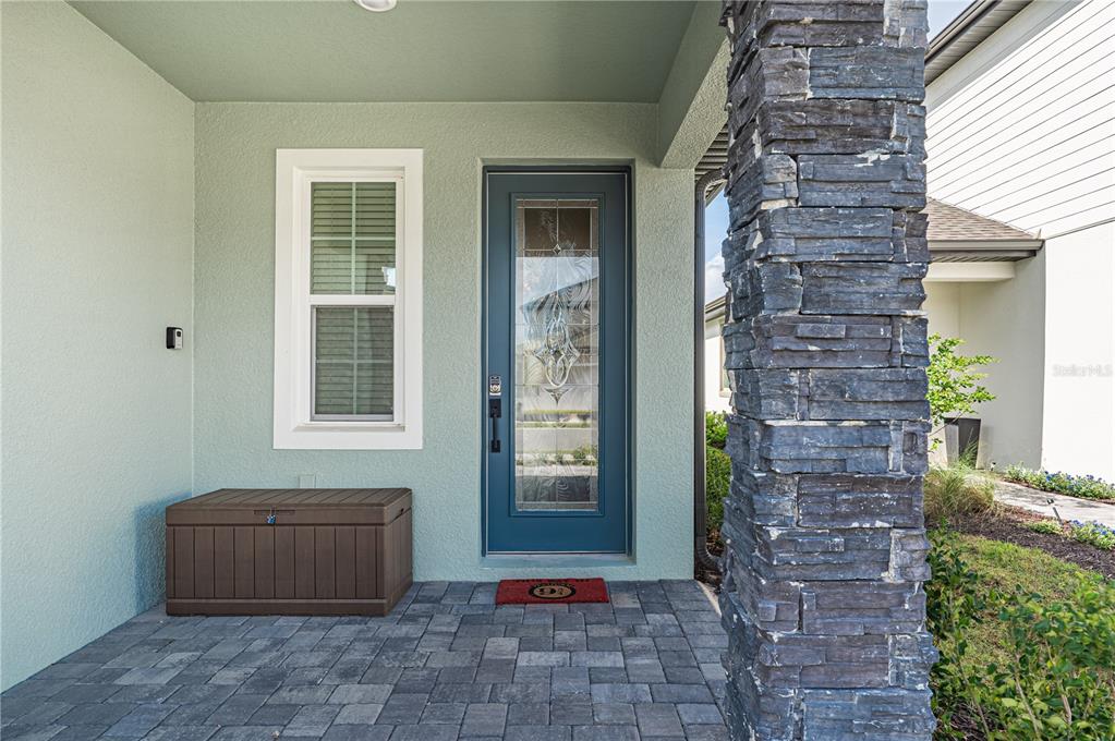 A front porch with a blue door, a window, a storage bin, and stone column — 7753 SOMERSWORTH DRIVE, KISSIMMEE, FL