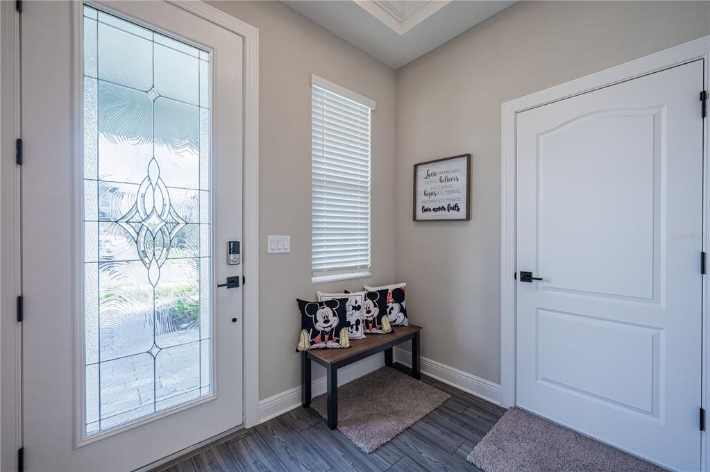 An entryway features a glass-paneled front door, a wooden bench with Mickey Mouse pillows, and flooring — 7753 SOMERSWORTH DRIVE, KISSIMMEE, FL