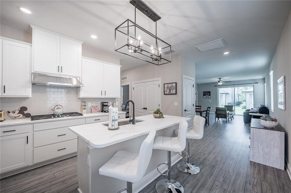 A modern kitchen features white cabinetry, a marble-topped island with bar stools, and wood flooring — 7753 SOMERSWORTH DRIVE, KISSIMMEE, FL