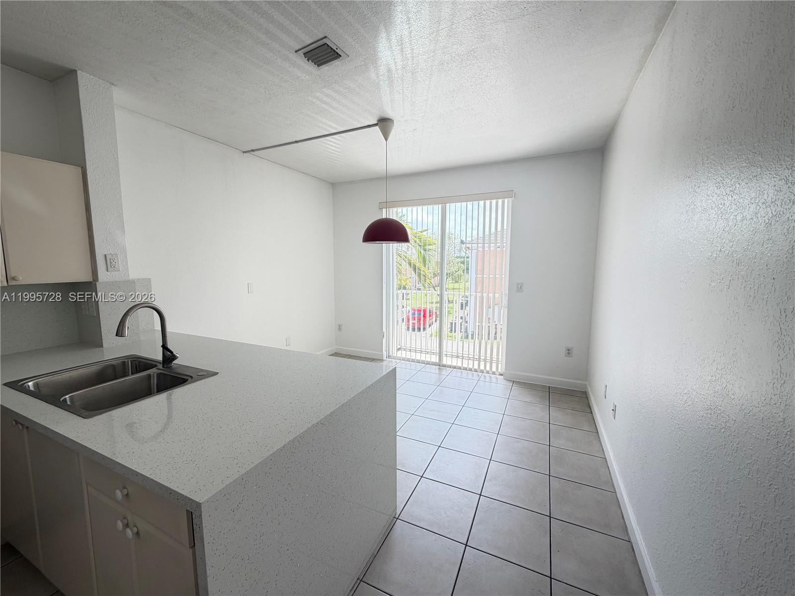 A kitchen island with a sink faces a dining area with tile floors and sliding doors — 7080 NW 177th St # 13, Hialeah FL 33015, HIALEAH, FL