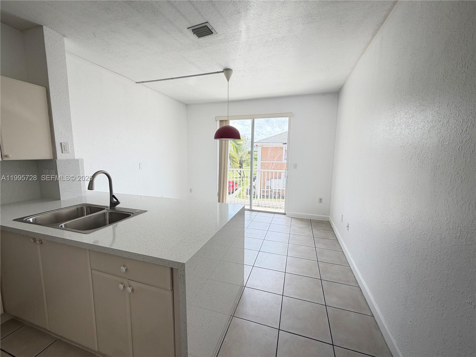 A kitchen island with a double sink faces a dining area with a sliding door — 7080 NW 177th St # 13, Hialeah FL 33015, HIALEAH, FL