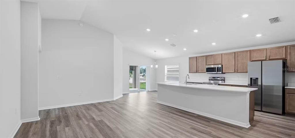 A kitchen with wood cabinets and stainless steel appliances opens to a living area — 35420 DARLINGTON GROVE DRIVE, ZEPHYRHILLS, FL