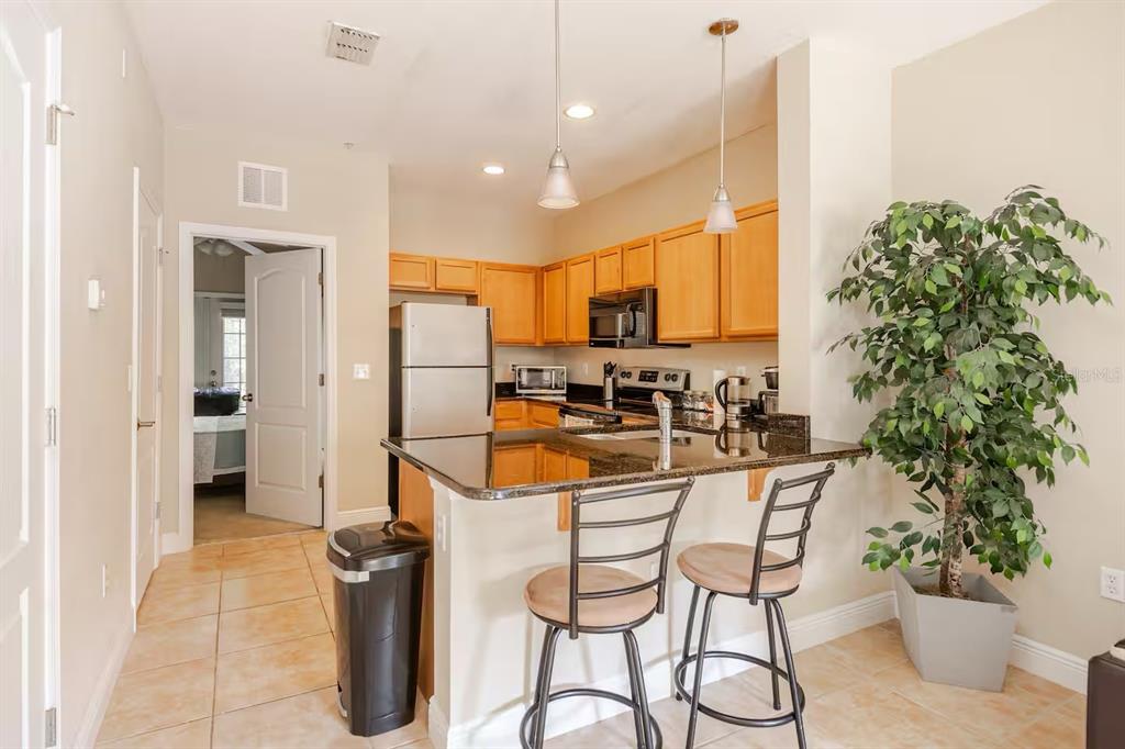 A kitchen with wooden cabinets, granite countertops, a breakfast bar, and two bar stools — 2960 SW 35TH PLACE UNIT 65, GAINESVILLE, FL