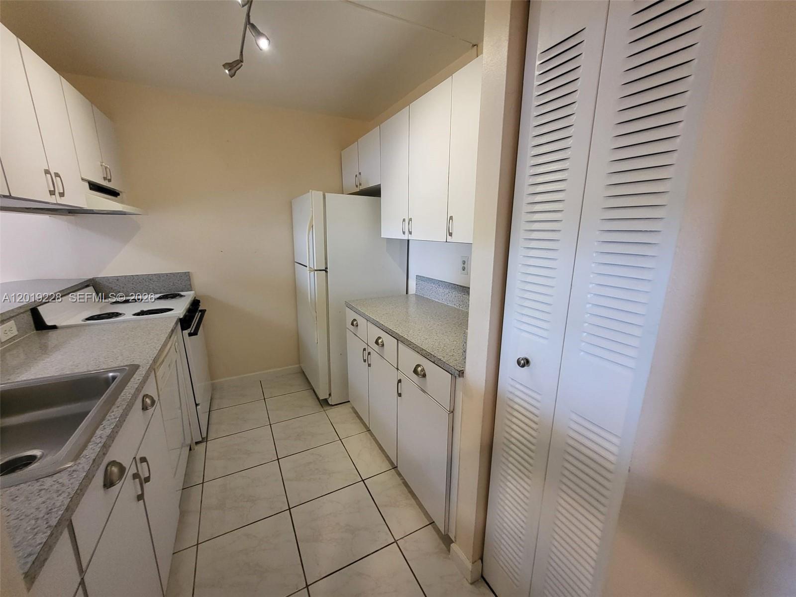 A galley kitchen features white cabinets, speckled countertops, white appliances, and light-colored tile flooring — 10801 SW 109th Ct # D305, Miami FL 33176, MIAMI, FL