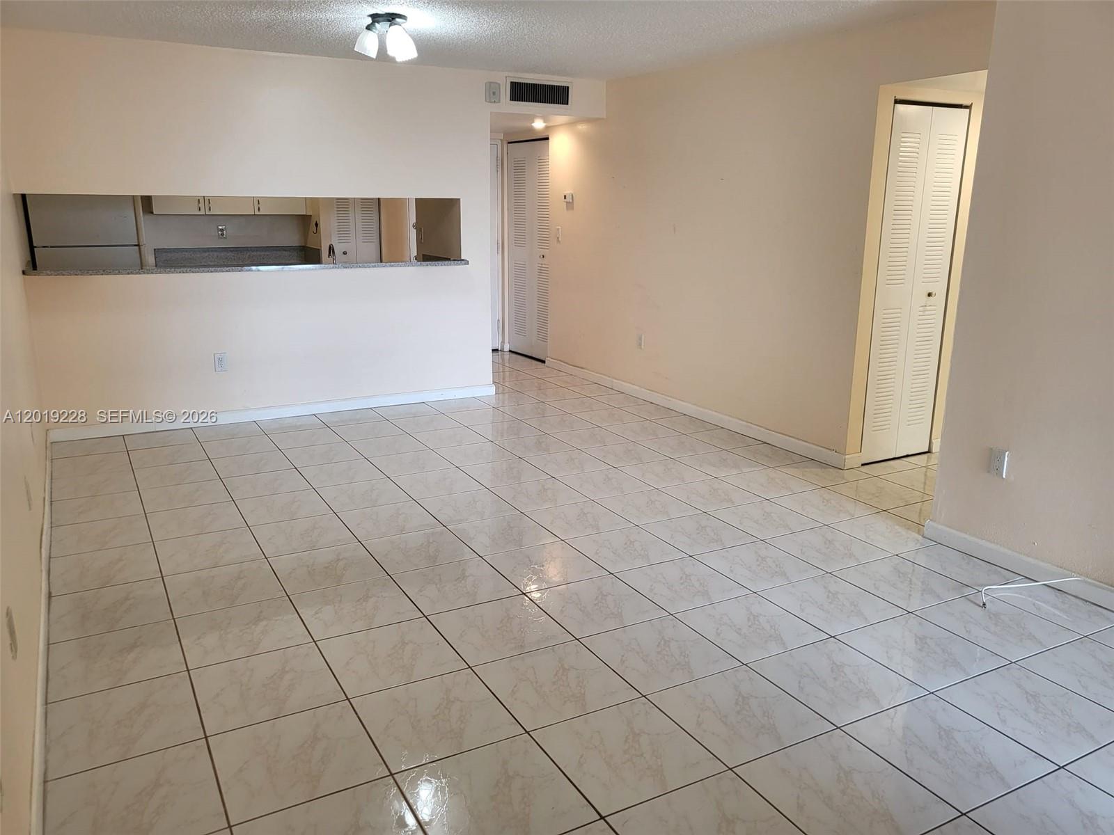 An empty room features light-colored tile flooring, a kitchen pass-through window, and white closet doors — 10801 SW 109th Ct # D305, Miami FL 33176, MIAMI, FL