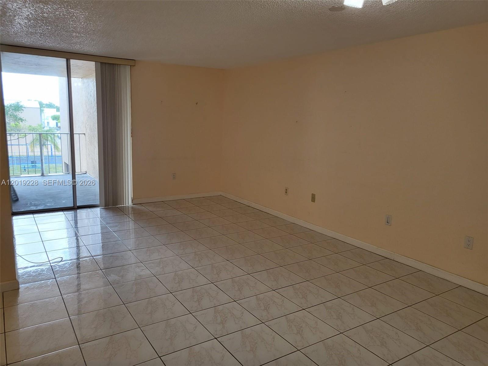 An empty room features beige walls, light-colored tiled floors, and a sliding glass balcony door — 10801 SW 109th Ct # D305, Miami FL 33176, MIAMI, FL